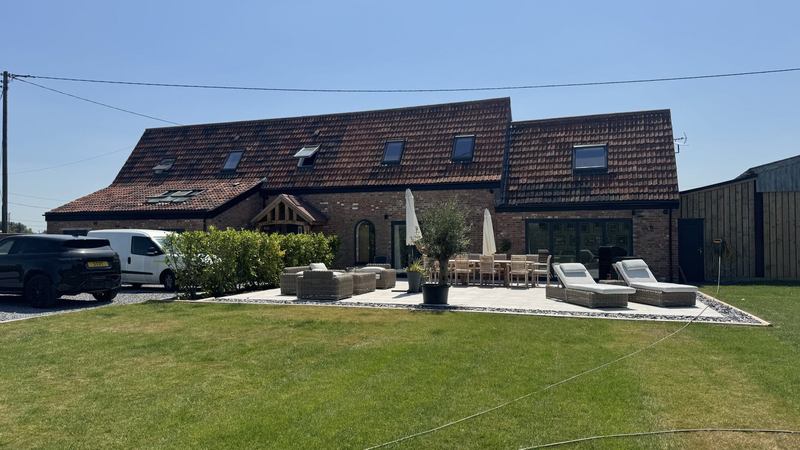 The same house after renovation, with a new tiled roof and dormer, glazed doors and a porcelain terrace laid out for dining and lounging