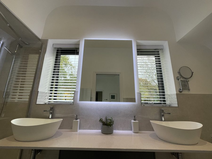 Renovated bathroom with twin basins, a backlit mirror and shuttered windows