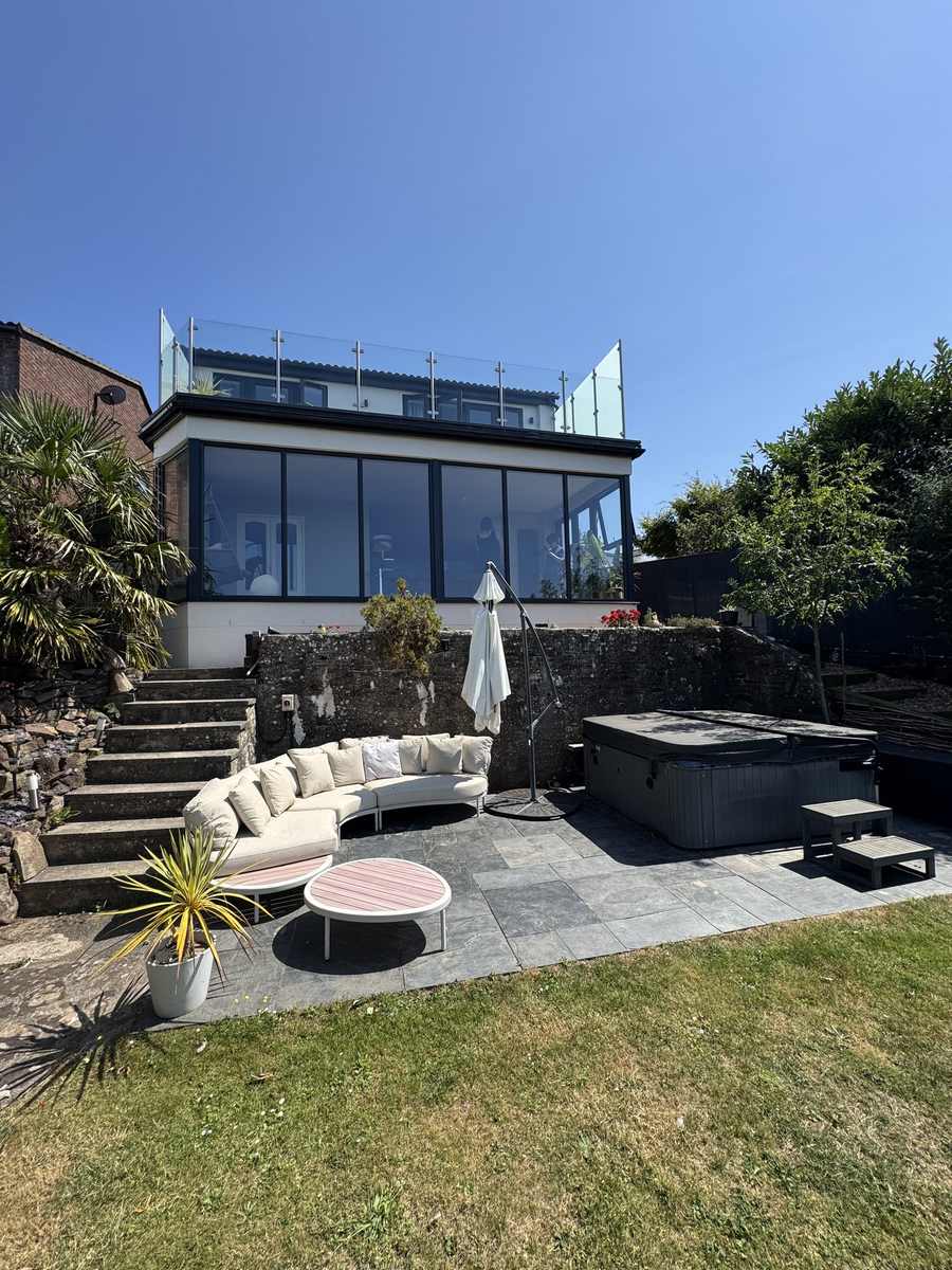 Landscaped rear garden with a paved terrace, hot tub and a glazed upper-floor extension above